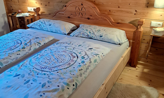 A cozy bedroom with a wooden bed and colorful bedding. The walls are made of wood, and there is soft light from the wall lamps.