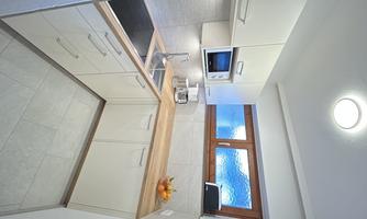 A modern kitchen with white cabinets and a wooden countertop. The large windows provide plenty of light and allow a view outside.