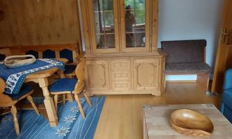 A cozy living space with a wooden cupboard and a dining table. The floor is made of light wood and there is a blue carpet.