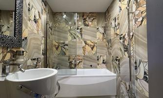 A modern bathroom with a bathtub and a glass shower. The walls are decorated with colorful, patterned tiles.