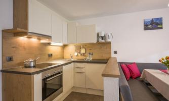 A modern kitchen with wooden and white elements. Fresh flowers are on a table and there is a cozy seating area.