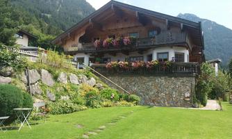 A charming house in alpine style with flower boxes and a well-kept garden. In the background, mountains can be seen that complete the landscape.