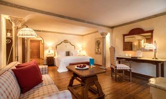 An elegantly furnished room with a large bed and cozy furniture. The room has warm light and stylish decorative elements.