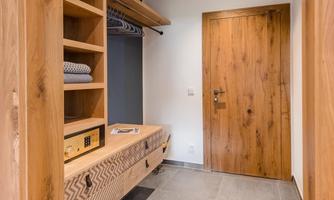 A modern hallway with wooden shelves and a wooden dresser. The door is made of dark wood and gives a warm, inviting impression.