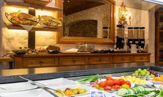 A rich breakfast buffet with fresh fruits, vegetables, and rolls. In the background, there are baskets and a mirror visible.