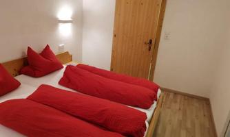 A cozy bedroom with two single beds and red bedcovers. The walls are light and the door is made of wood.