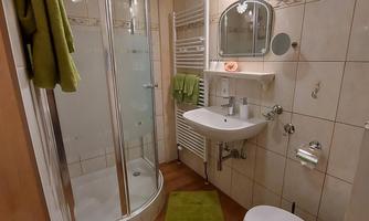 A modern bathroom with a shower cubicle and a sink. There are bright tiles and a green carpet.