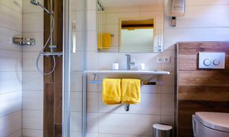A modern bathroom with a shower and a sink. Yellow towels hang on the wall and there is a bright, friendly atmosphere.