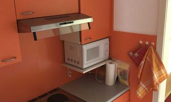 A small kitchen with orange cabinets and a modern stove. In the background, a microwave and a refrigerator door are visible.