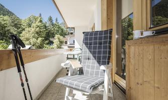 A cozy balcony with a comfortable chair and a view of green trees. On the table sits a cup, perfect for relaxed moments outdoors.