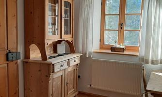 A cozy room with a wooden floor. There is a wooden cupboard and a window with curtains.