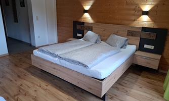 A cozy bedroom with a large double bed and wooden paneling. Soft lighting and a simple design create a relaxed atmosphere.