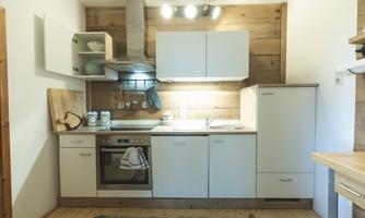 A modern kitchen with wood and white elements. It features a stove, a sink, and storage space.