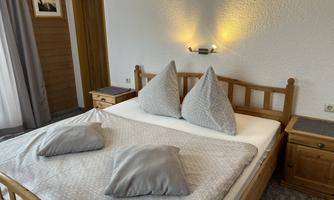 A cozy bedroom with a wooden bed and gray pillows. The walls are light and the room is brightly lit.