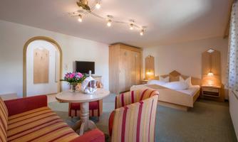 A cozy room with a double bed, a table, and two chairs. The decor is modern and friendly, featuring soft lighting elements.