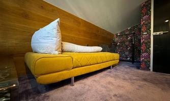 A modern yellow sofa stands in a cozy room. The walls are adorned with colorful floral designs.