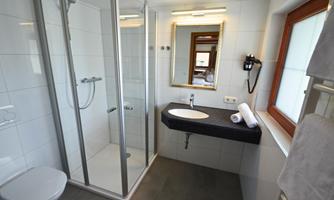 A modern bathroom with a shower, a sink, and a large mirror. The walls are brightly tiled, and the bathroom feels clean and well-lit.