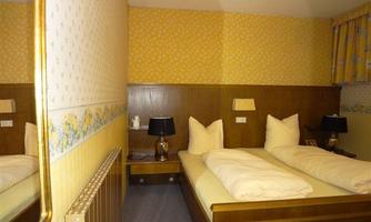 A cozy bedroom with two single beds, wooden paneling, and yellow walls. Black table lamps are on the nightstands, and there is a large mirror on the wall.