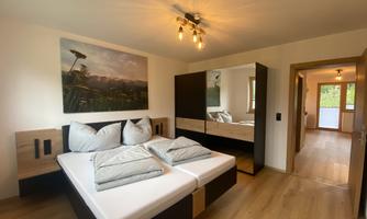 A modern bedroom with a double bed and a large mirrored dresser. The room is bright and inviting, with a window that leads to a balcony.