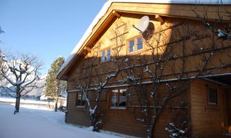 A cozy wooden house in the snow with a bright sky.  
Surrounded by snow-covered trees and a peaceful winter landscape.