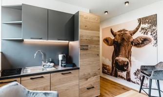 A modern kitchen with wooden and gray cabinets. A large picture of a cow hangs on the wall.