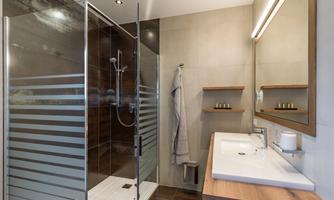 A modern bathroom with a glass shower and a stylish sink. On the wall, there are wooden shelves with personal care products.