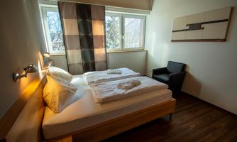 A cozy bedroom with two single beds and modern furniture. The room has large windows and a calm atmosphere.