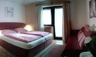 A cozy bedroom with a large double bed and a red sofa. The room has windows with curtains and is tastefully furnished.