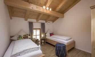 A cozy room with two single beds and a wooden ceiling. Natural light enters the room through the window.