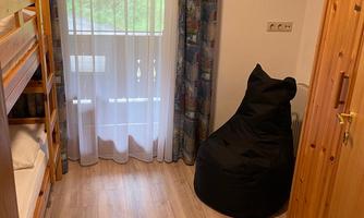 A cozy room with a bunk bed and a bean bag. The windows let in plenty of light and offer a view of nature.