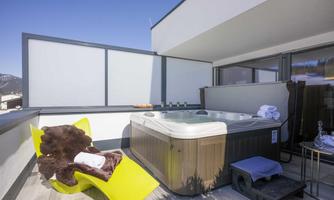 An elegant balcony with a hot tub and a cozy lounge chair. The clear view and modern style create a relaxing atmosphere.