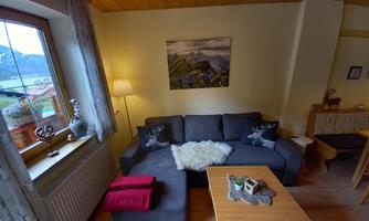 A cozy living room with a gray sofa and a wooden table. Large windows let in plenty of light and offer a view of the mountains.