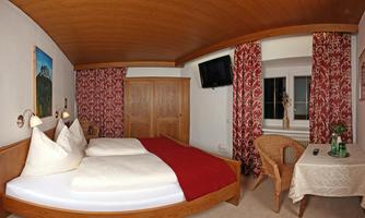 A cozy bedroom with a double bed and traditional decorations. The room has a television and a small table with chairs.