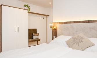 A modern bedroom with a large bed and a cozy seating area. The room has light walls and warm lighting for an inviting atmosphere.