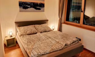 A cozy bedroom with a large bed and modern lamps. Through the window, there is a beautiful view of the mountains.