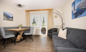A modern living room with a cozy couch and a dining area. Large windows let in plenty of daylight and offer a view of nature.