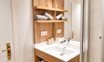 A modern bathroom with wooden shelves and fresh towels. The sink is designed to be simple and elegant.