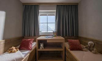 A cozy children's room with two beds and colorful cushions. A beautiful view of the mountains is visible through the window.