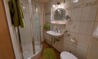 A modern bathroom with a shower, sink, and toilet. The walls are tiled, and there are green towels.