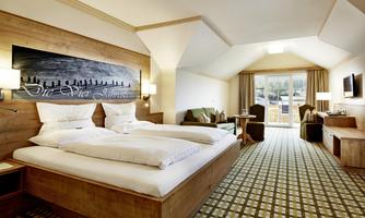 A modernly furnished hotel room with two beds and wood paneling. It offers a cozy atmosphere and a balcony with an outdoor view.