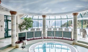 An elegant spa area with a round jacuzzi and large windows. The view of nature and the bright decor create a relaxing atmosphere.