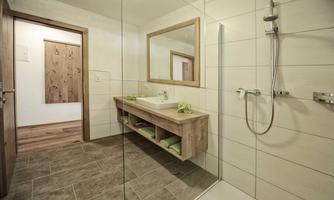 A modern bathroom with a walk-in shower and a large mirror. Wooden furniture and green towels create a cozy atmosphere.