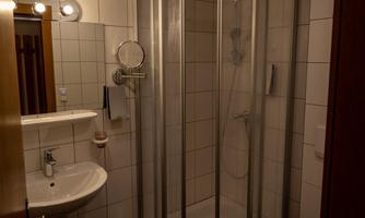 A small bathroom with a shower cubicle, sink, and toilet. The walls are tiled and the light is bright.