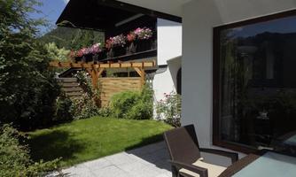 A beautiful garden with green grass and colorful flowers. In the background, there is a house with a balcony.