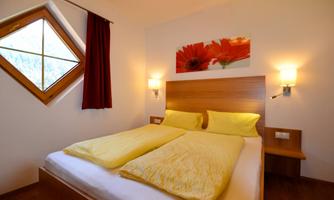 A cozy bedroom with a double bed and yellow bedcovers. The room has a decorative window and is equipped with warm lighting.