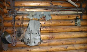 A rustic wooden wall with various equipment items. A backpack, helmets, and a lamp are hanging on it.