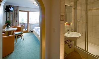 A comfortable hotel room area with a table and chairs, as well as a bathroom with a shower. The room is well-lit and offers a pleasant atmosphere.