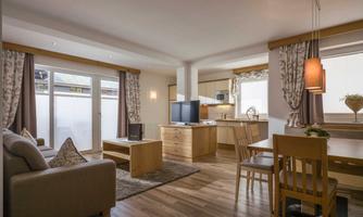 A modern living room with wooden furniture and a cozy sofa.  
Large windows provide plenty of light and are ideal for a relaxed atmosphere.