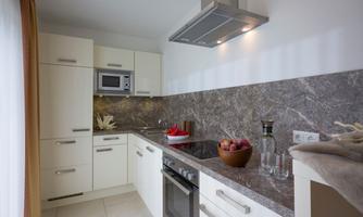 A modern kitchen with white cabinets and an elegant marble countertop. The equipment includes a stove, a microwave, and fresh fruit in a bowl.