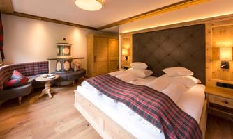 A cozy bedroom with a large bed and wooden ceilings. The room is stylishly furnished with a seating area and warm light.
